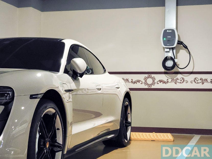 一輛白色電動跑車停在室內車位，牆上安裝有電動車充電設備。